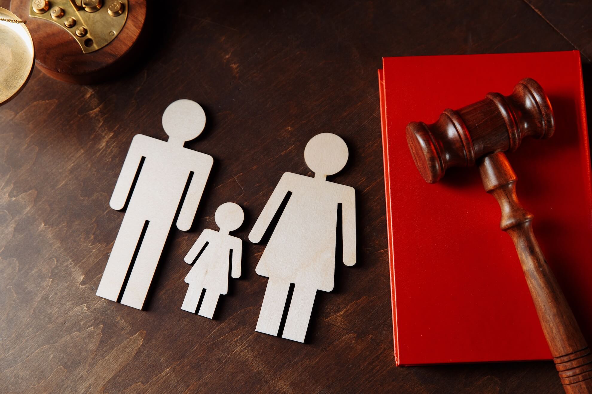 Sobre una superficie de madera se colocan figuras de madera de una familia y un mazo junto a un libro rojo. Derecho Civil. Elena Giménez Abogada.