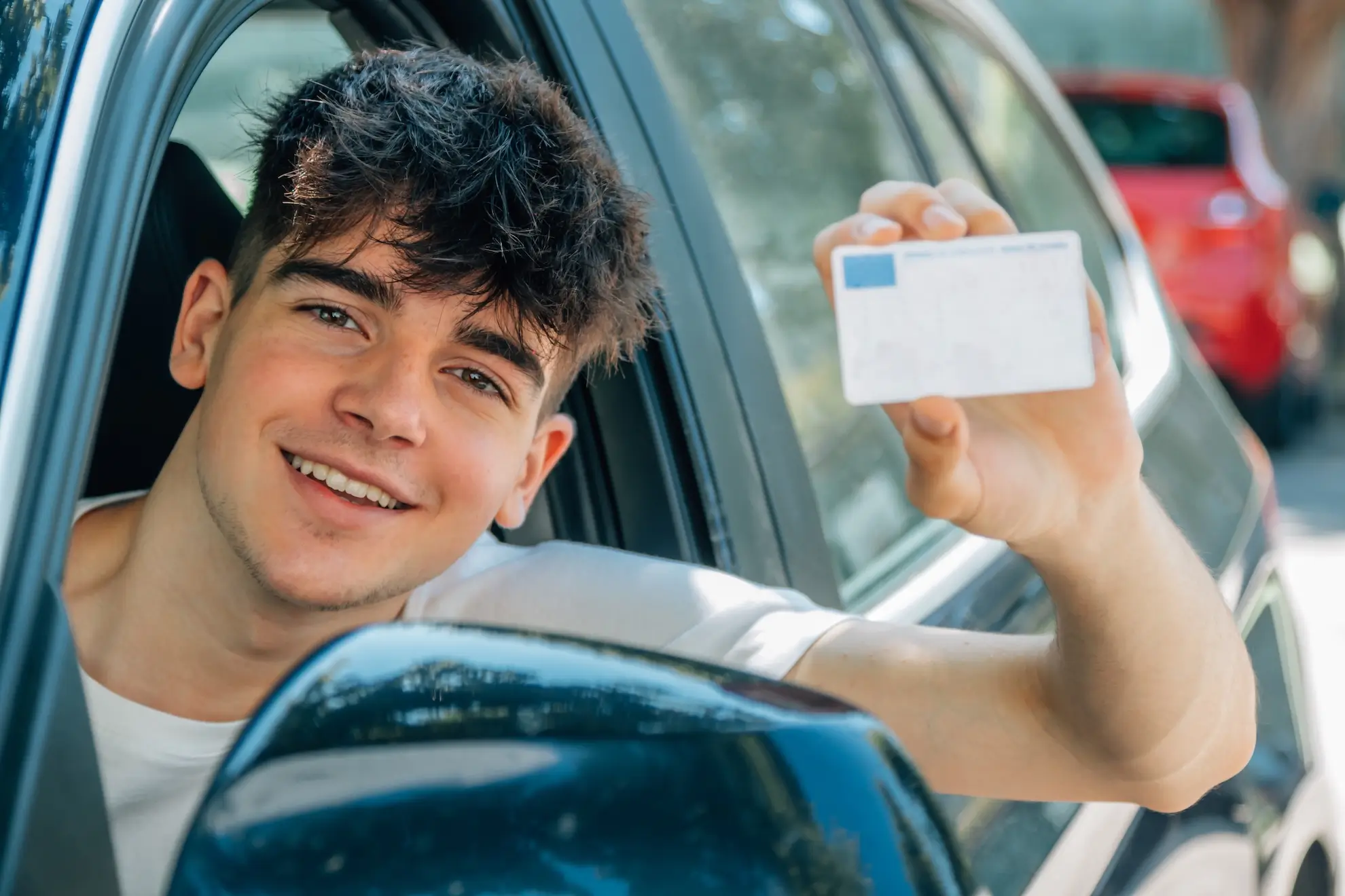 Un joven sentado en un automóvil sostiene una tarjeta y sonríe. conducir permiso extranjero