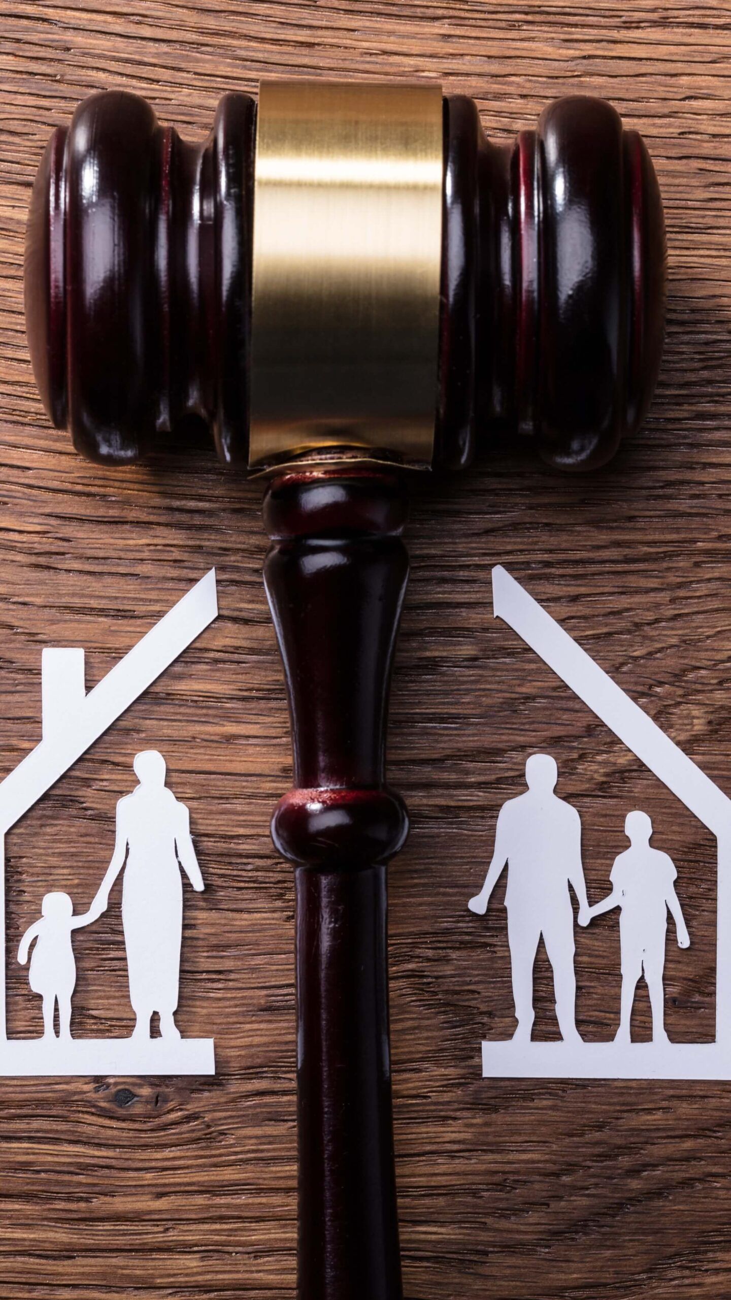 Un mazo de madera entre dos figuras de papel: una de un hombre y un niño, y la otra de una mujer y un niño, que representan una decisión familiar.