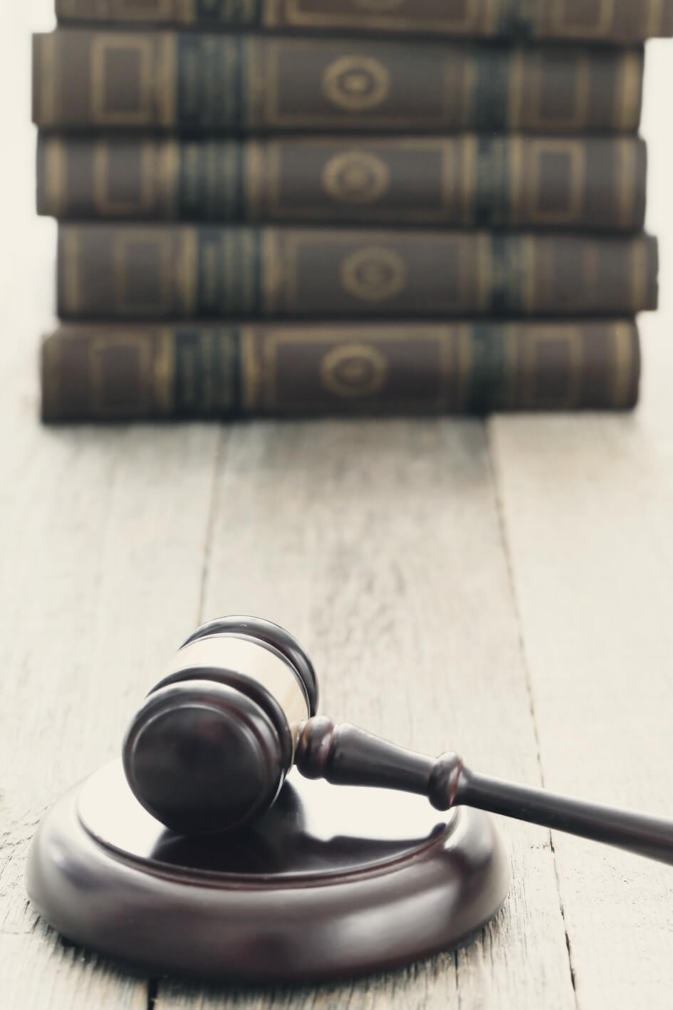 En primer plano, un mazo de madera reposa sobre su base y en el fondo, sobre una superficie de madera clara, hay una pila de libros de leyes.