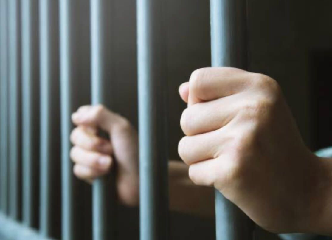 Manos agarrando los barrotes de una celda de prisión, iluminación tenue.permisos de salida penitenciarios