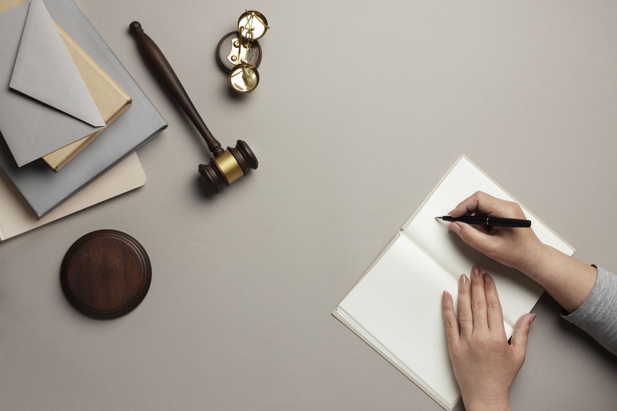 Manos escribiendo en un cuaderno sobre un escritorio con sobres, un mazo, un bloque de sondeo y un par de gafas. Servicios Jurídicos Elena Giménez Abogada